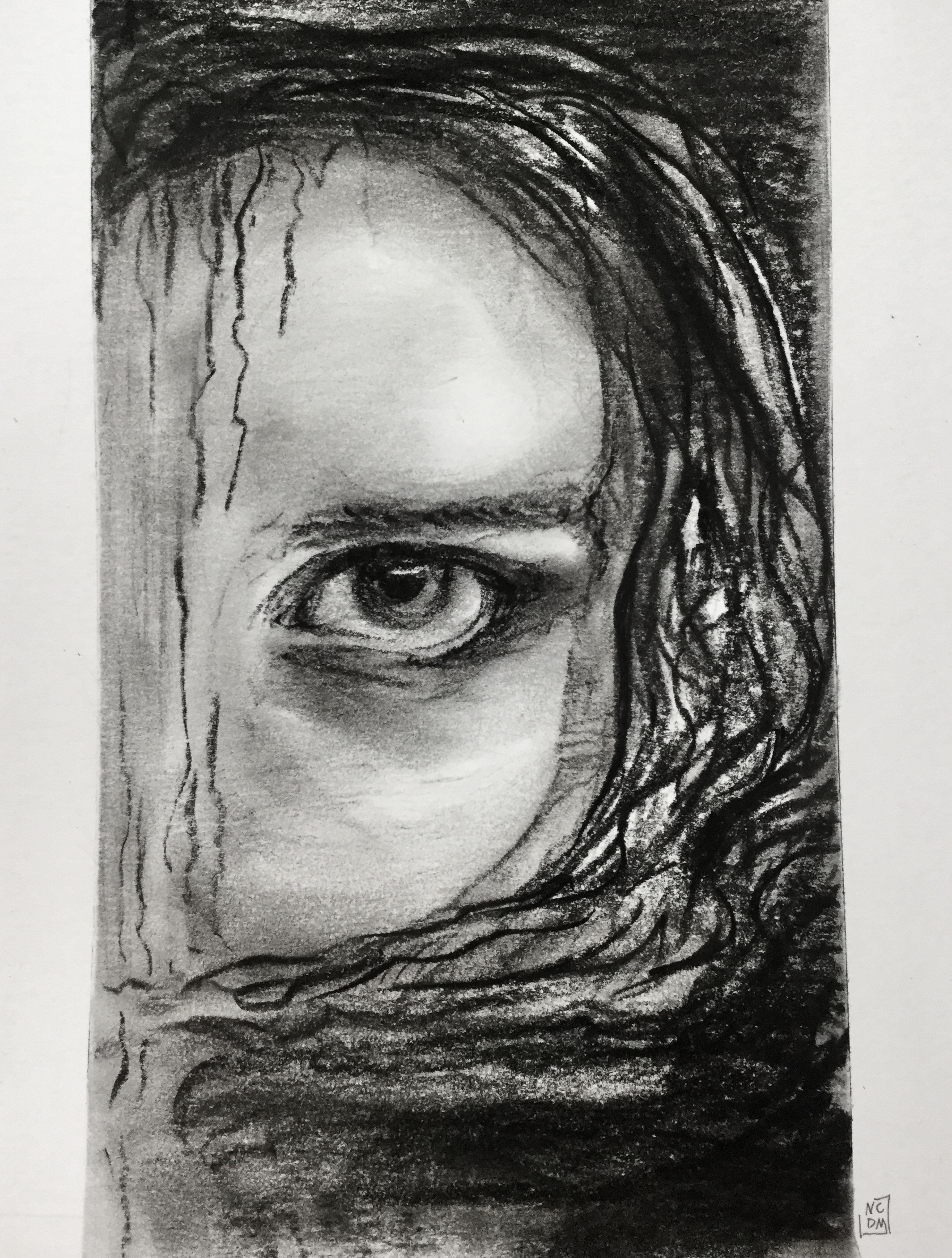 Charcoal drawing of a woman's eye looking up at you with a quiet rage in her eye, her hair spills to the side and fills the page with darkness